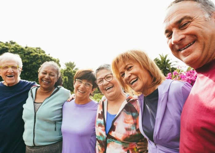 Multiracial senior people having fun hugging each other after sport workout at city park - Healthy lifestyle and joyful elderly lifestyle concept - Main focus on right woman face