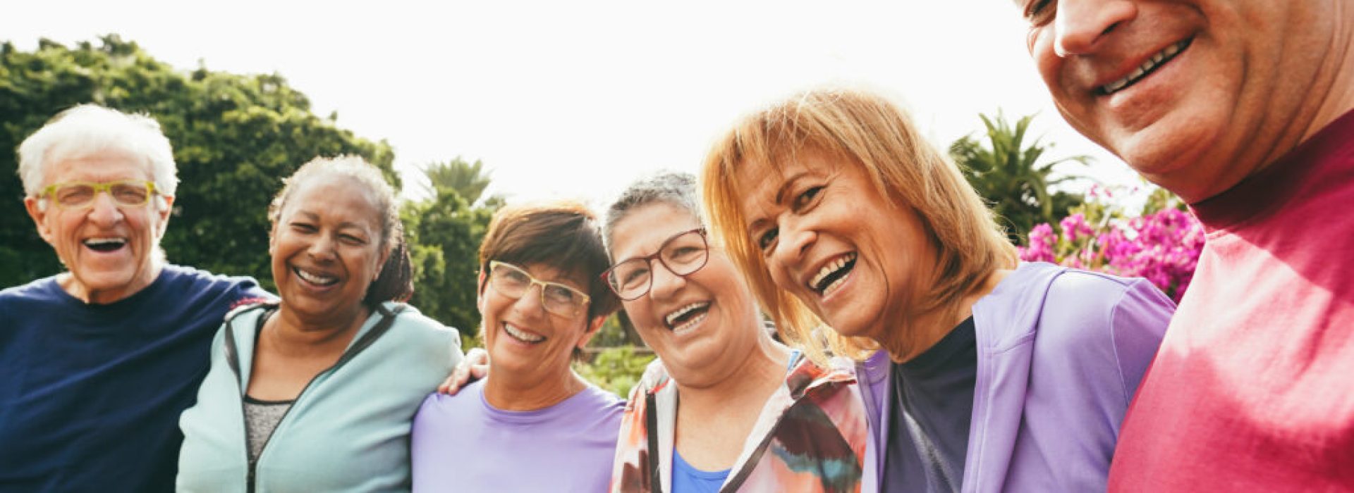 Multiracial senior people having fun hugging each other after sport workout at city park - Healthy lifestyle and joyful elderly lifestyle concept - Main focus on right woman face